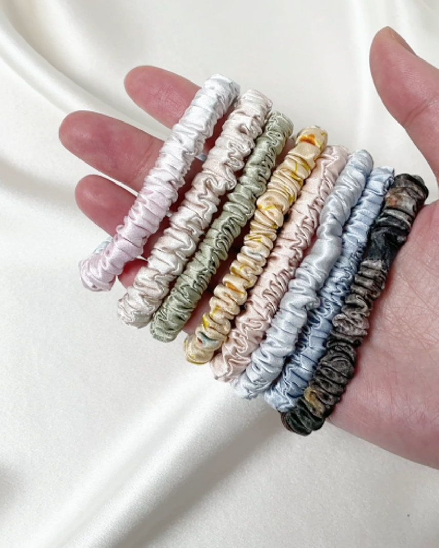 Silk scrunchies shown in a hand across multiple stock colors